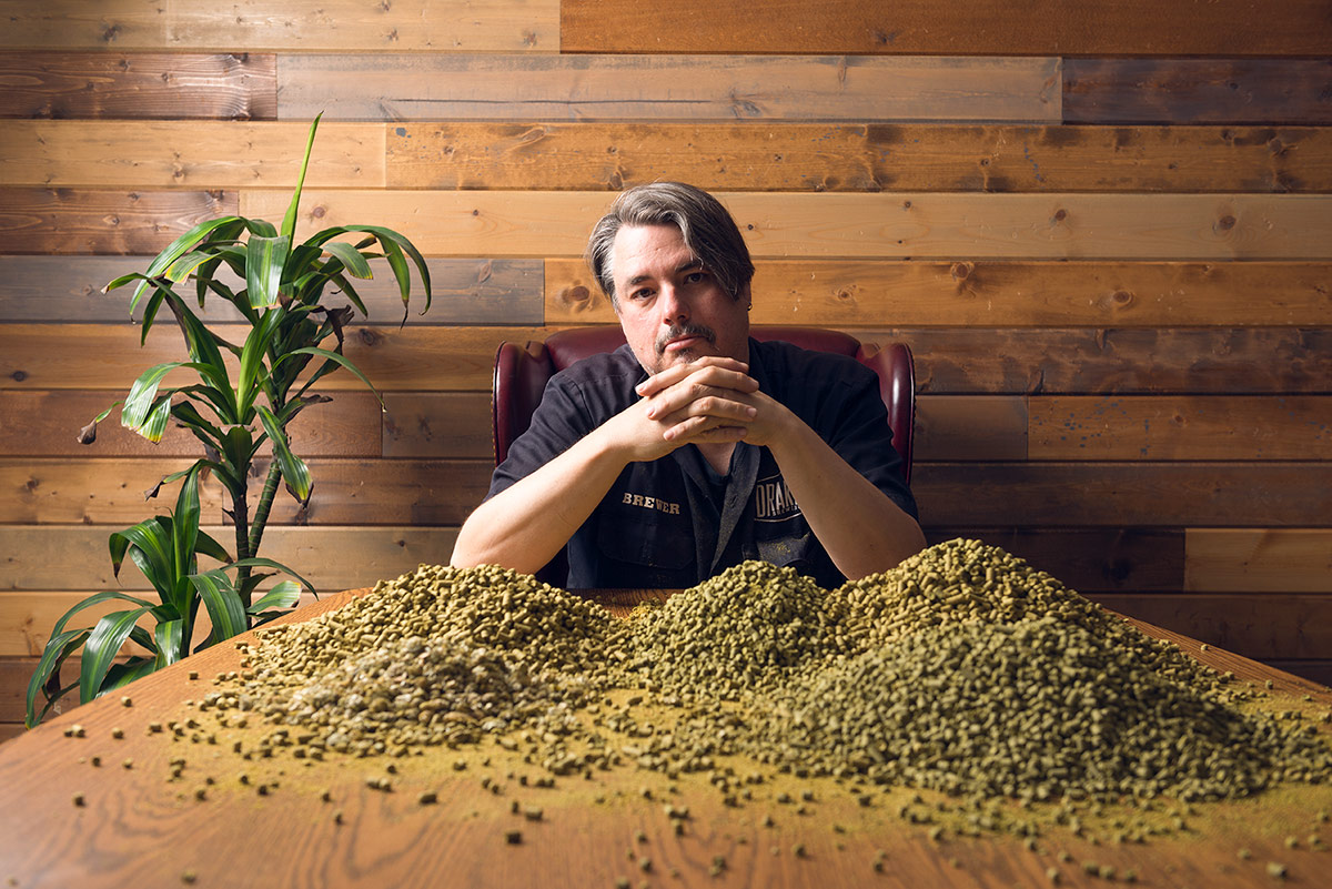 Brewmaster John Gillooly sitting at a table behind a giant pile of hop pellets
