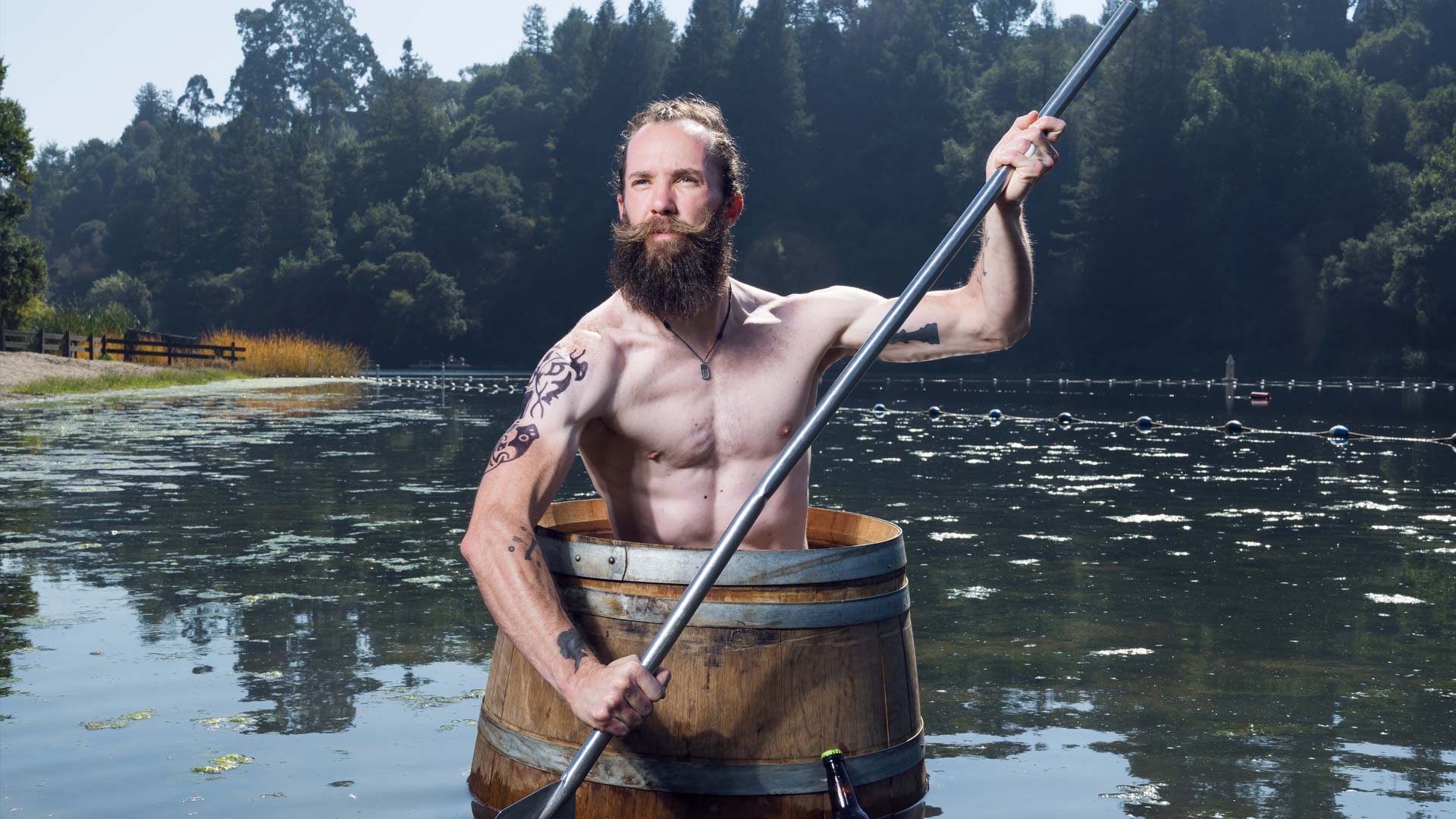 Brewer Chris seated and paddling in a beer barrel floating in a pond