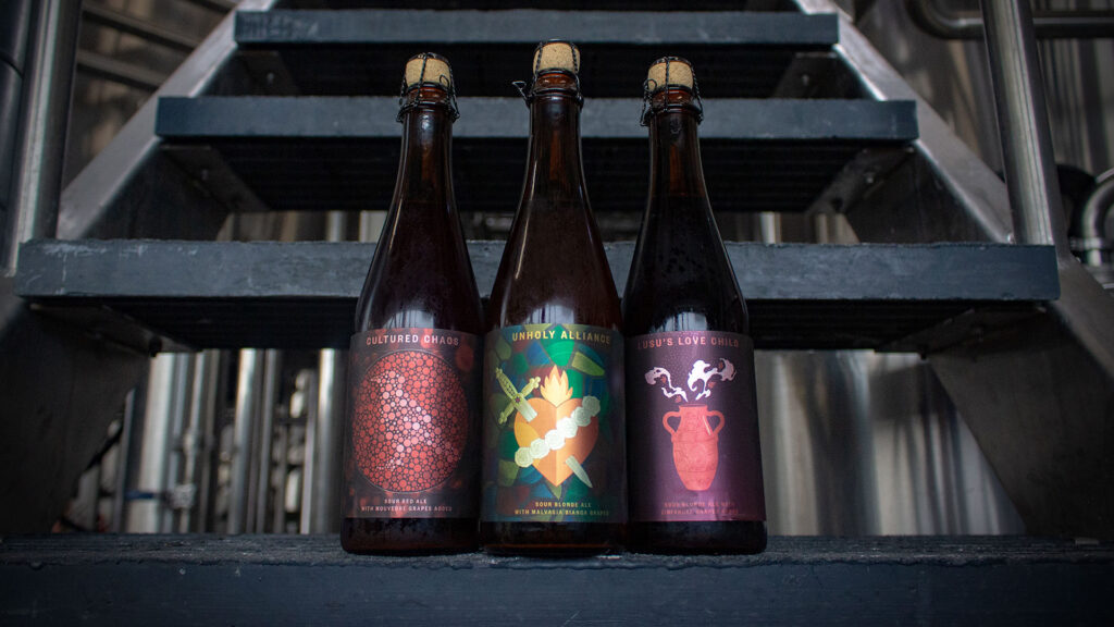 Three bottled beers sitting on the brewhouse stairs: Unholy Alliance, Lusu's Love Child, and Cultured Chaos