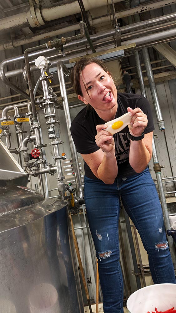Woman with tongue out holds egg in brewery