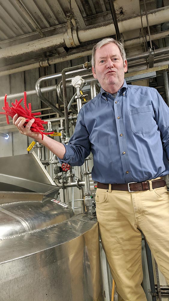 Man in blue shirt holds red licorice sticks in brewery