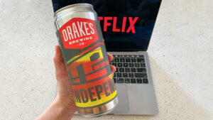 Hand holds Drake's Brewing Co. can in front of Netflix laptop