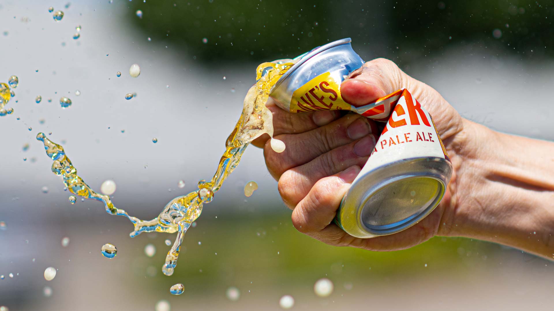 A hand crushing a can of Kick Back IPA