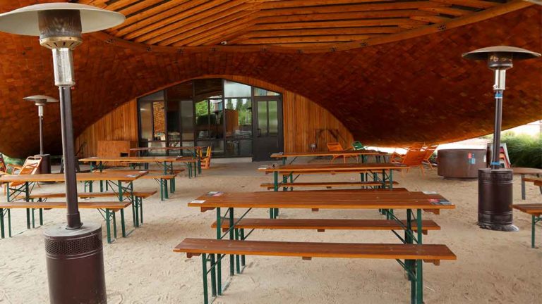 Picnic tables and heat lamps located underneath the overhang of the BARN building