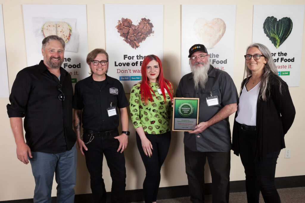 Five people pose for a photo, one holding an award plaque