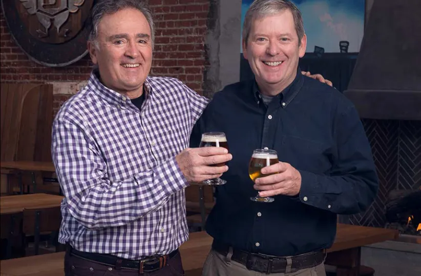 Two smiling men in a brewery toasting with beer
