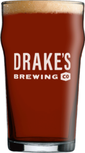 A pint glass filled with dark amber beer labeled "Drake's Brewing Co" on a white background