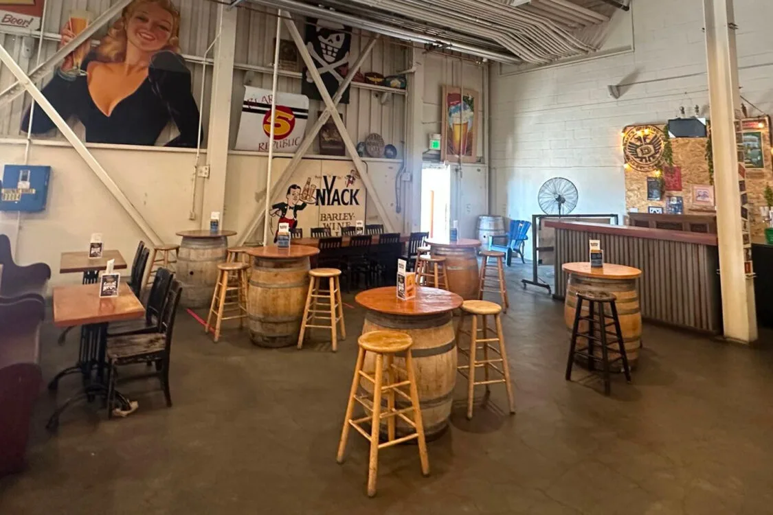 Rustic bar with barrel tables and stools, featuring a large portrait and brewery decor