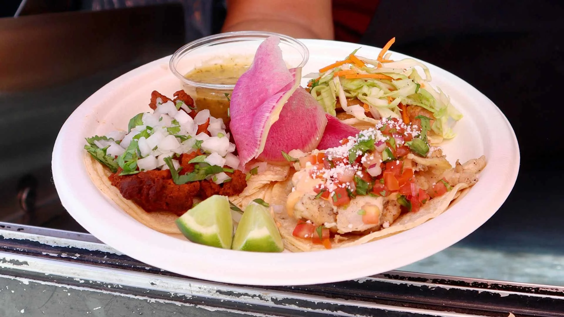 Plate of three authentic Mexican tacos with toppings and lime wedges