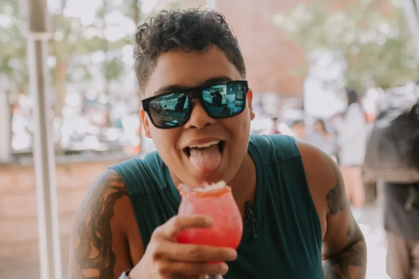 Person with sunglasses sticking tongue out holding a pink cocktail