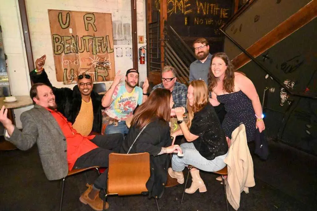 Group of friends posing for a photo at an event, with "UR BEAUTIFUL" sign