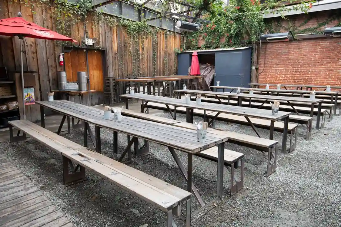 Outdoor seating area with long wooden picnic tables and benches, rustic wooden fence background