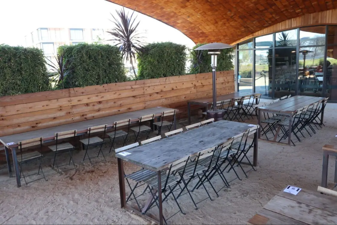 Outdoor seating area with long wooden tables and chairs under a curved roof