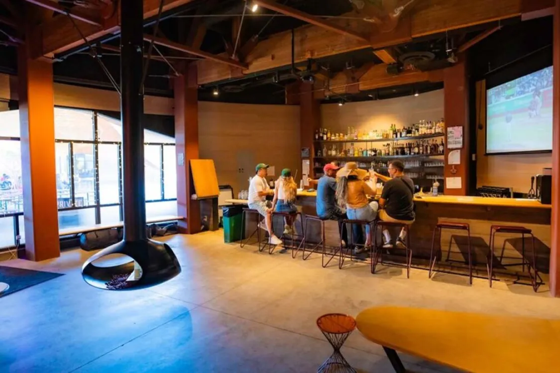 People seated at a bar in a modern restaurant with a hanging fireplace