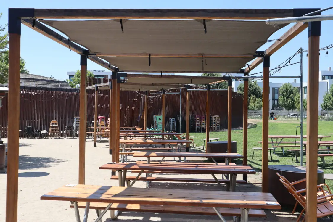 Outdoor picnic tables under a shaded canopy at a restaurant or beer garden